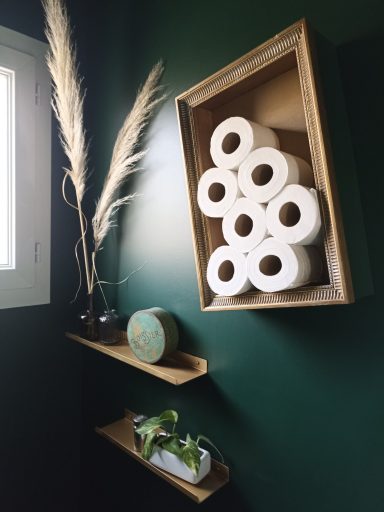 Un cadre chiné doré est upcyclé en réserve de papier toilette, quelques plumeaux de pampa apportent une touche végétale.